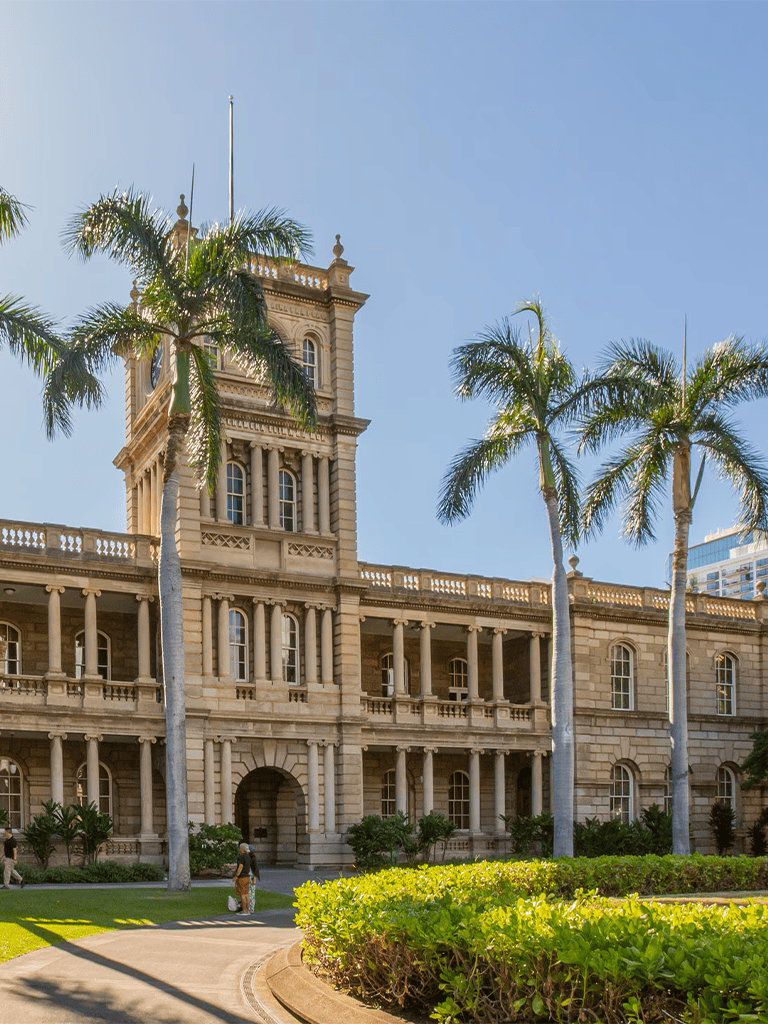 Historic government building with palm trees and lush greenery in sunny outdoor setting.