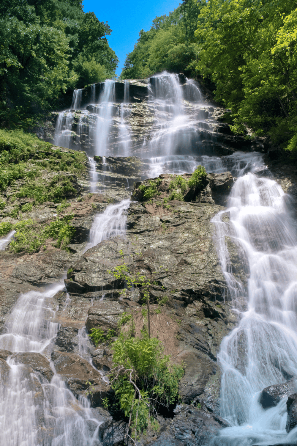 Serene waterfall cascading through lush green trees in a scenic natural landscape, perfect for adventure and outdoor exploration.