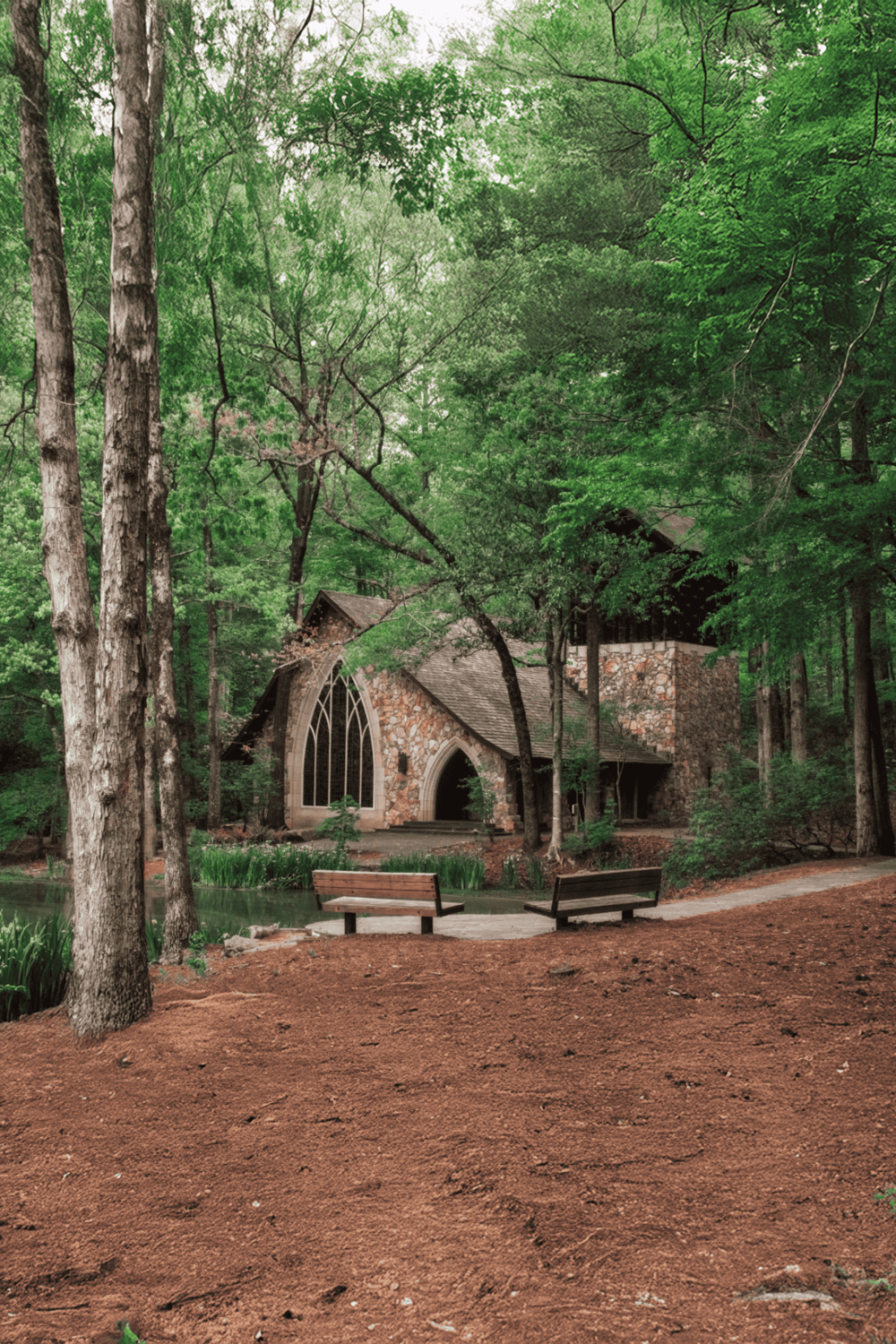 Serene forest chapel surrounded by lush green trees and tranquil pond, perfect for nature-inspired events.