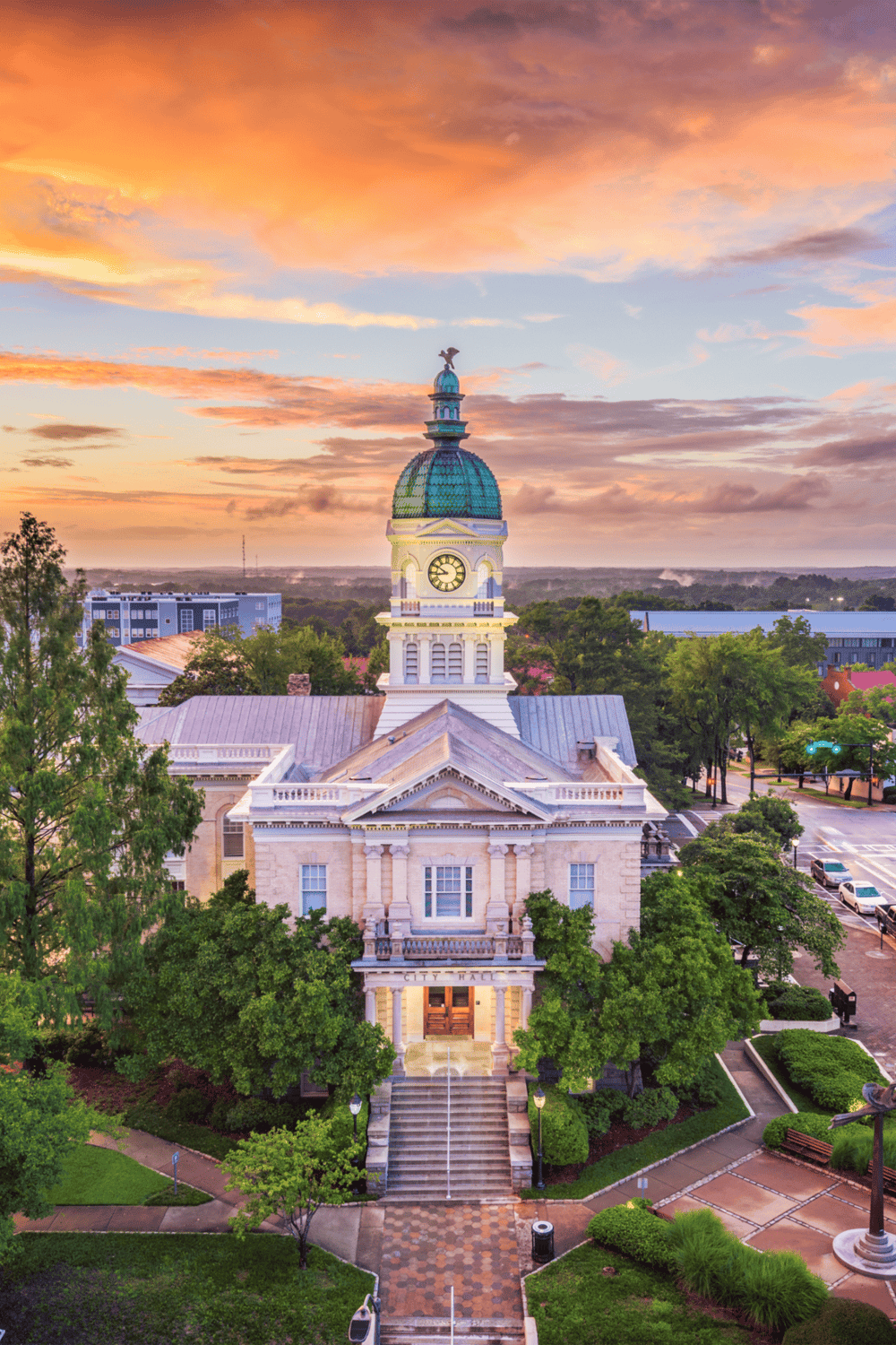 Historic city hall building with clock tower at sunset, vibrant sky and lush greenery, focus on local landmarks and architecture.