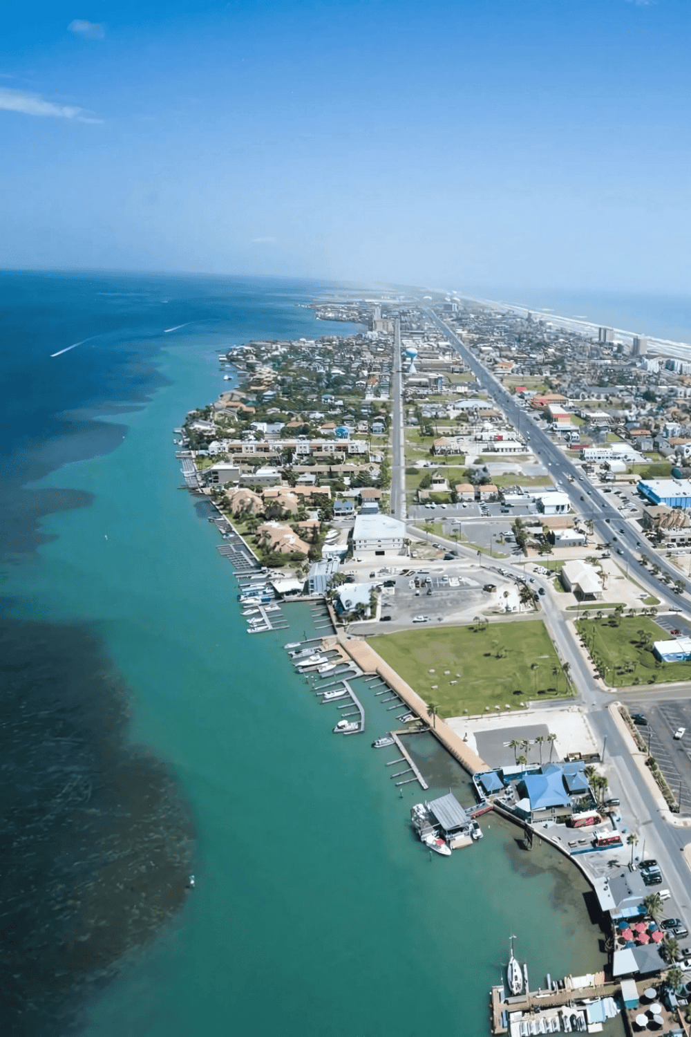 Aerial view of beachside city with marina and ocean, showcasing vacation destinations and coastal attractions.