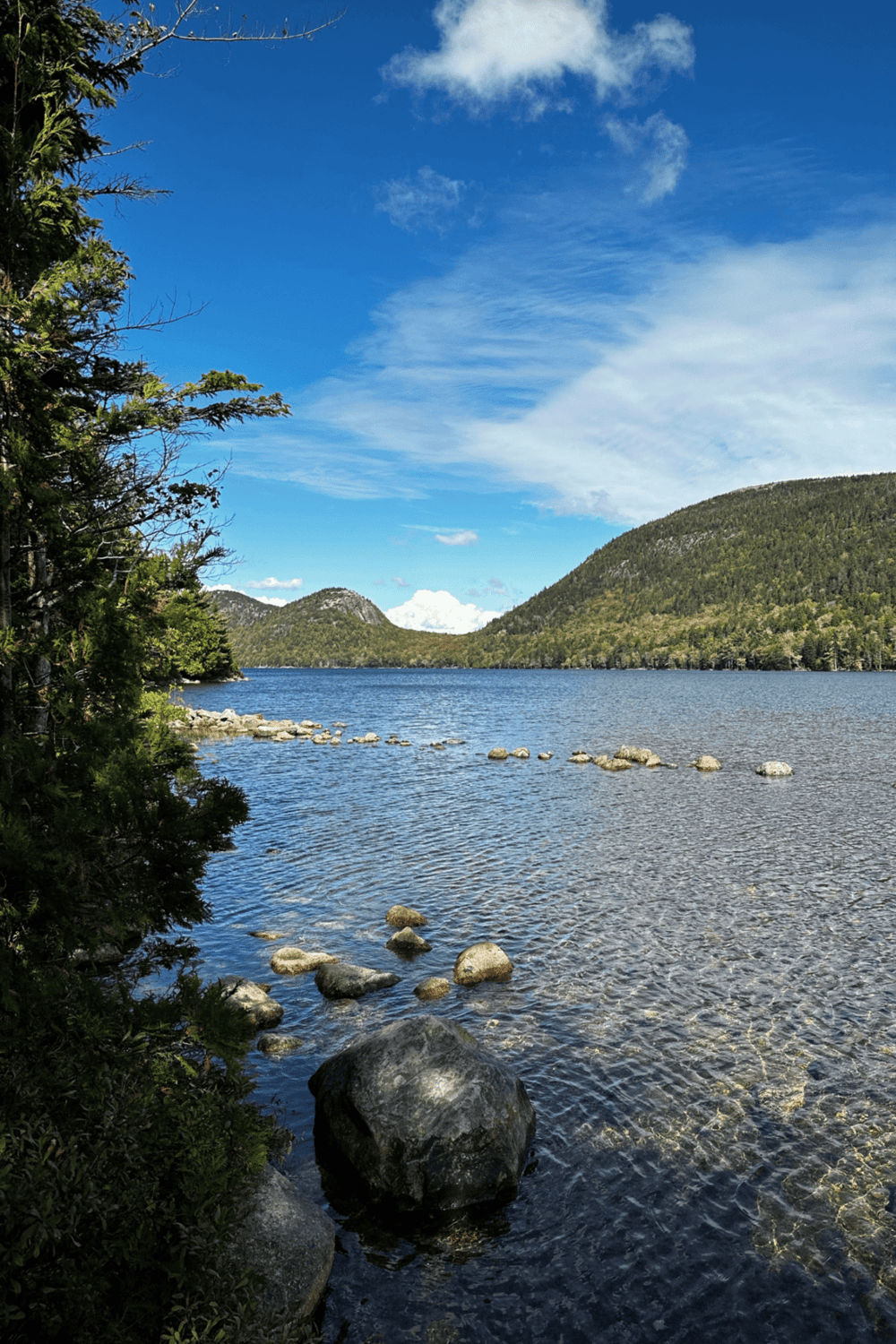 Serene mountain lake with clear water, surrounded by lush greenery and scenic hills.