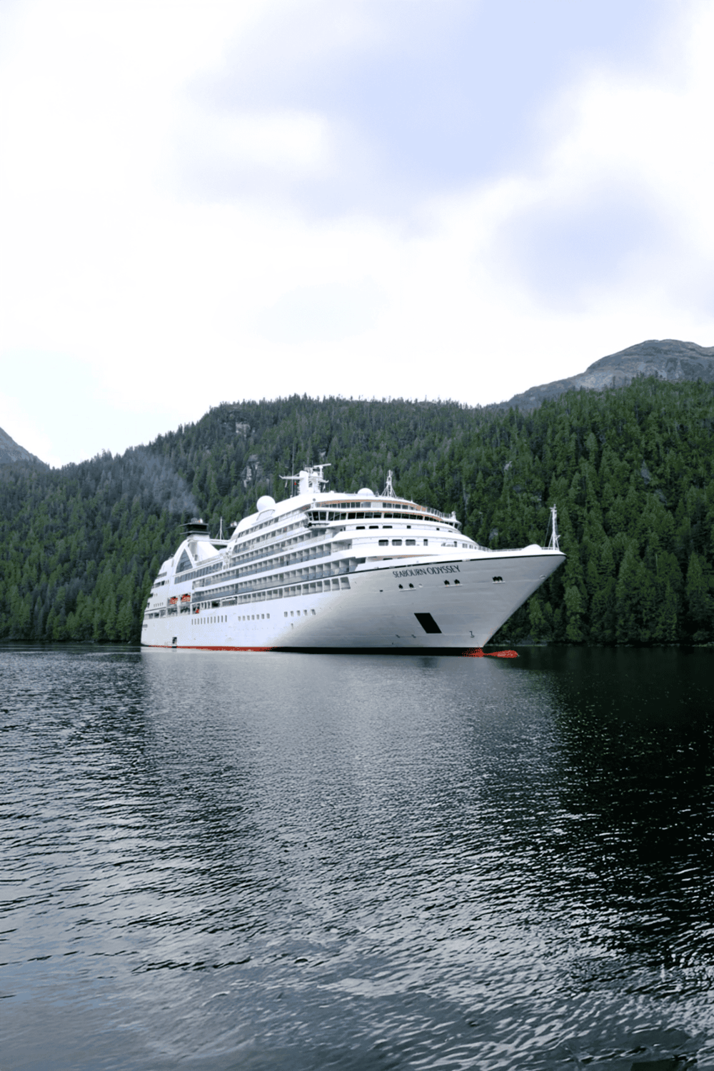 Luxury cruise ship sailing through scenic waters surrounded by green mountains.