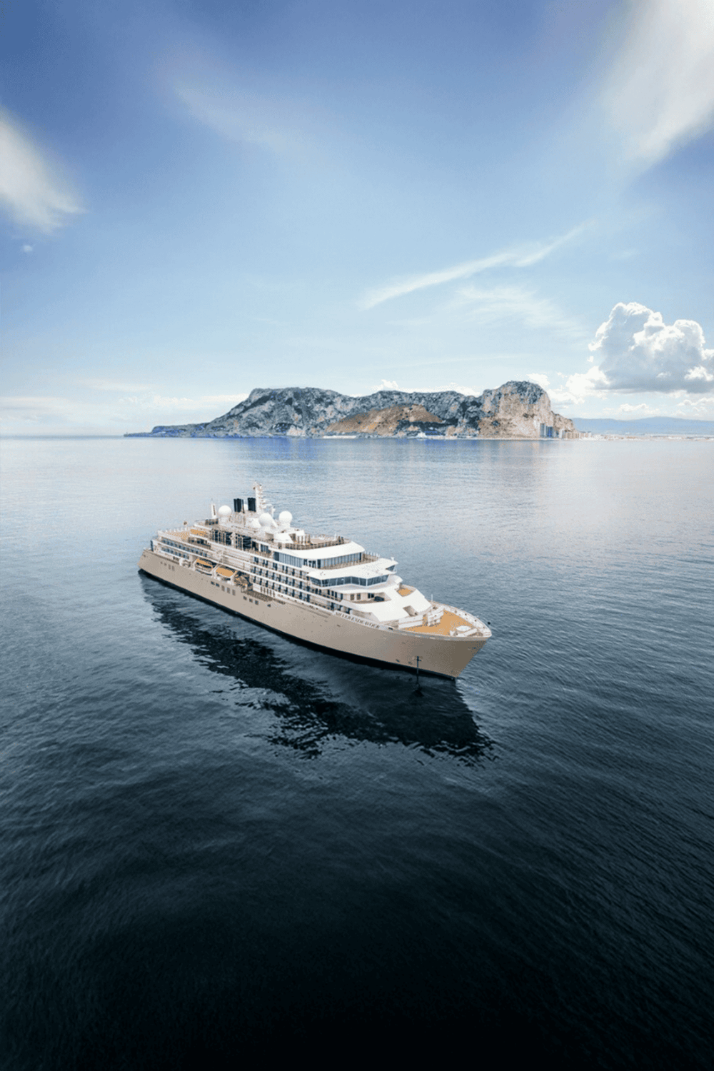 Luxury cruise ship sailing near island with cliffs, scenic ocean view, and blue sky.