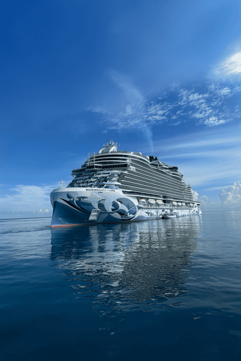 Luxury cruise ship Norwegian Prima on calm blue ocean under sunny sky.