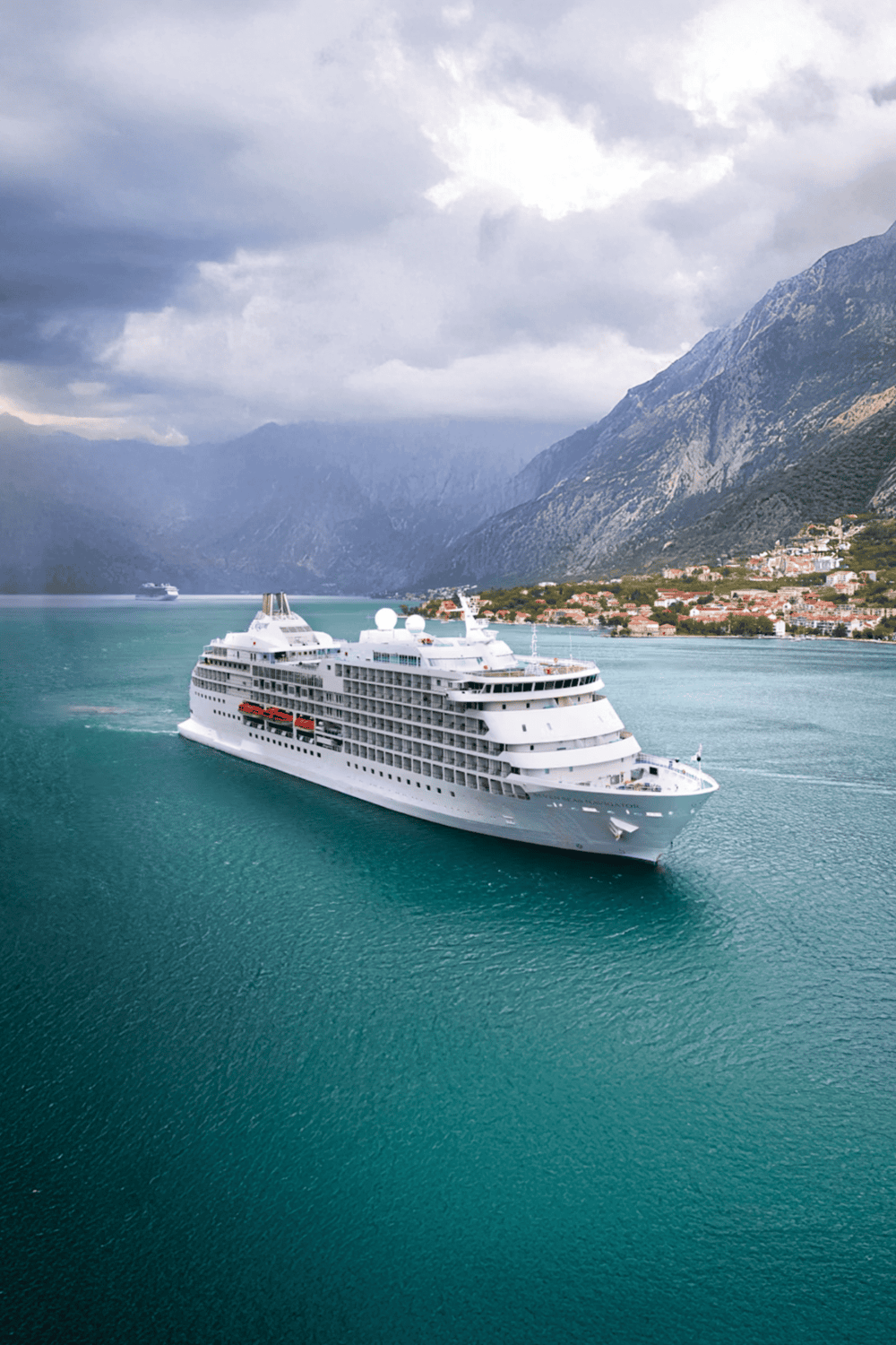 Cruise ship sailing through scenic fjord with mountains in the background.