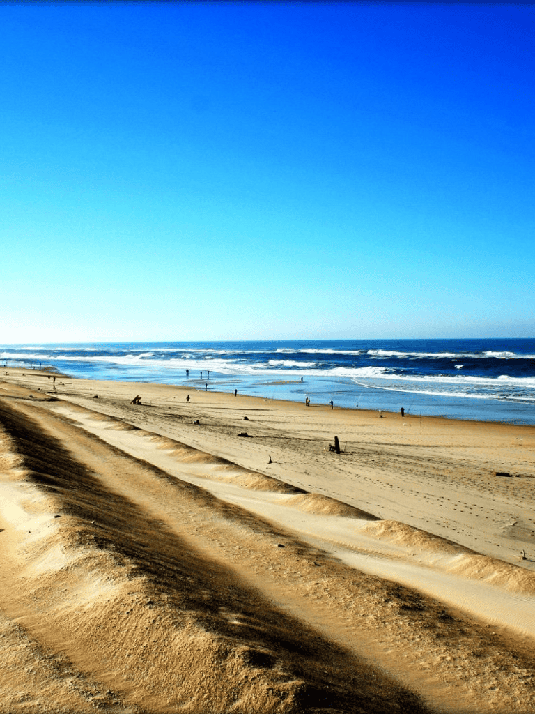 Wide sandy beach with ocean waves and clear blue sky.