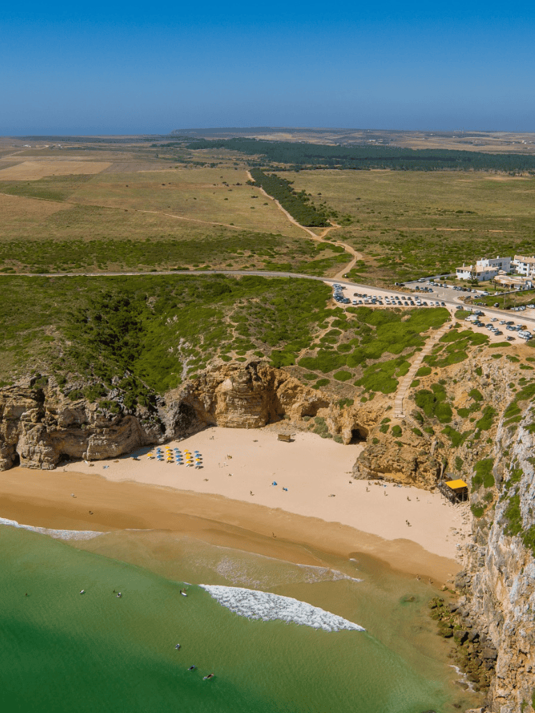 Seaside cove with sandy beach, coastal cliffs, and vibrant green waters, perfect for relaxing and surfing.