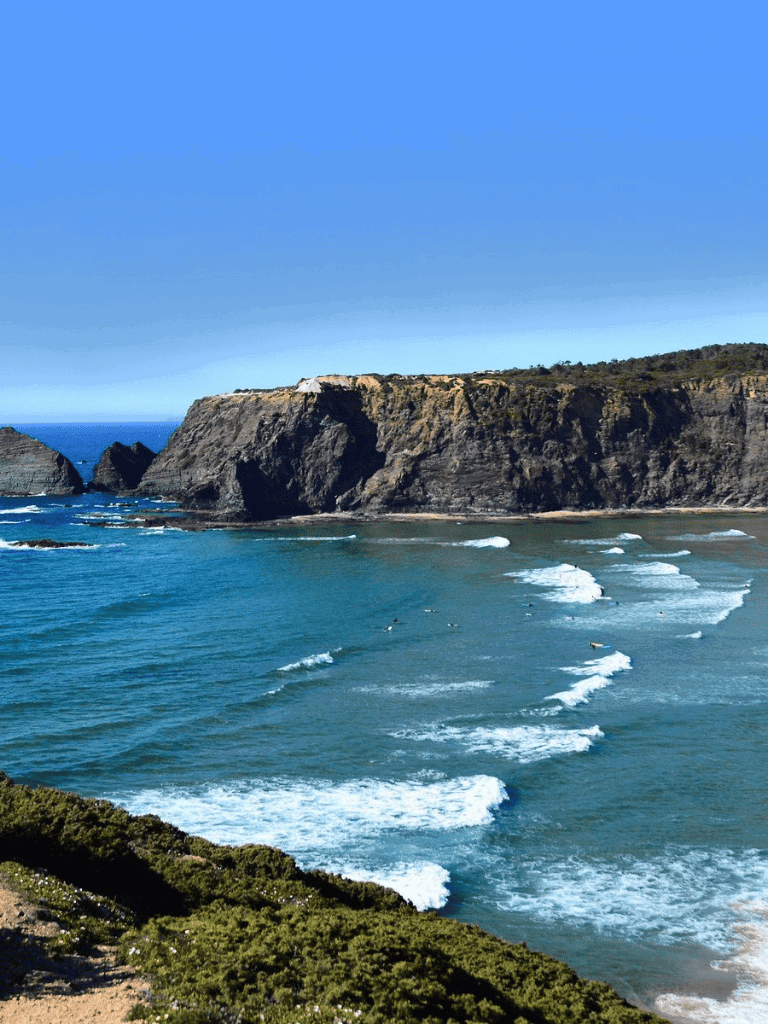 Vibrant coastal cliffs overlooking an ocean with gentle waves and clear blue sky.