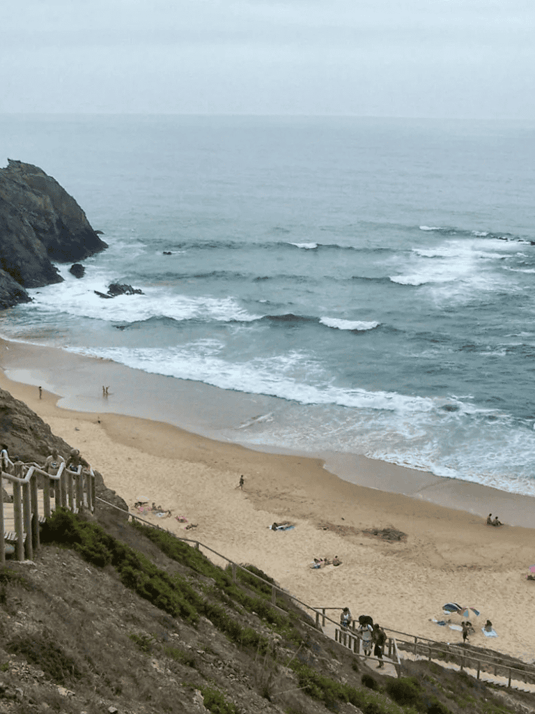 Secluded beach with cliffs, sandy shore, and visitors enjoying the ocean view and relaxing on the sand.