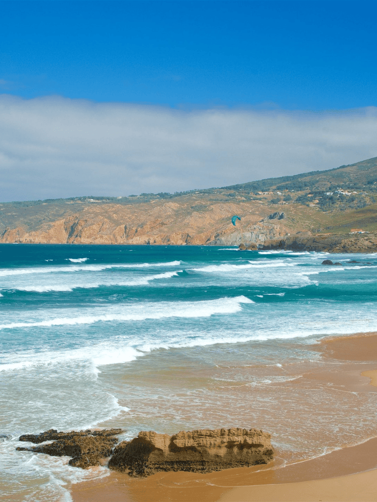 Vibrant beach with cliffs, waves, and a kite surfer under a blue sky, perfect for seaside adventure and navigation.