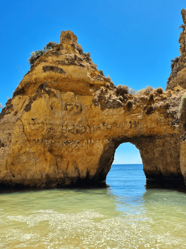 Seaside natural rock arch formation on sunny day with clear water and blue sky.