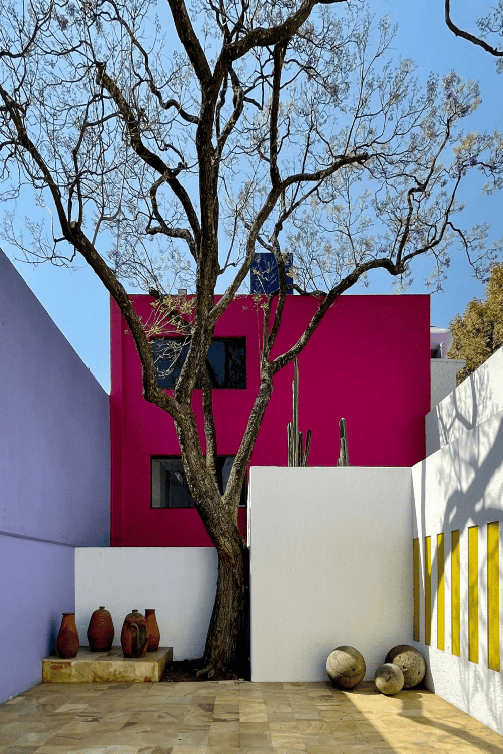 Vibrant pink and white modern architecture with a large tree, desert decor, and blue sky in the background.