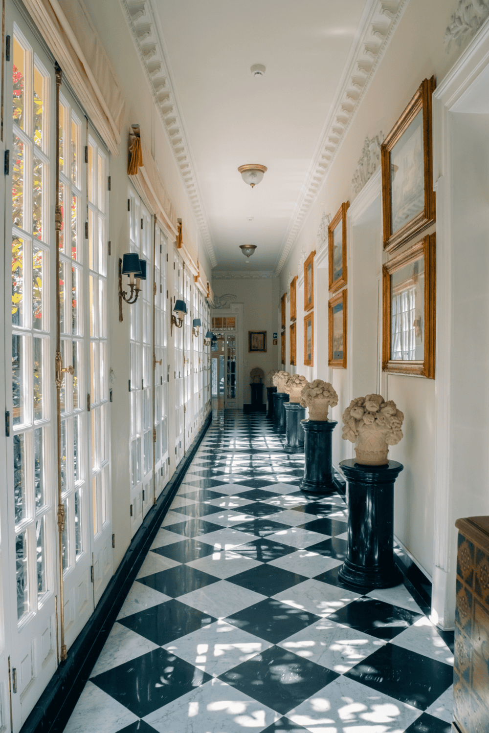 Elegant interior corridor with black and white checkered marble flooring, ornate wall decor, and vintage lighting fixtures.