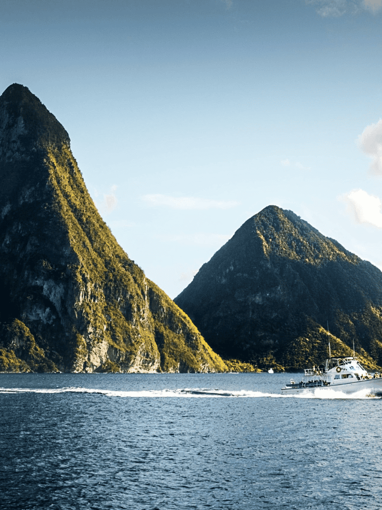 Bright blue water with a boat cruising past lush green mountain peaks at sunset.