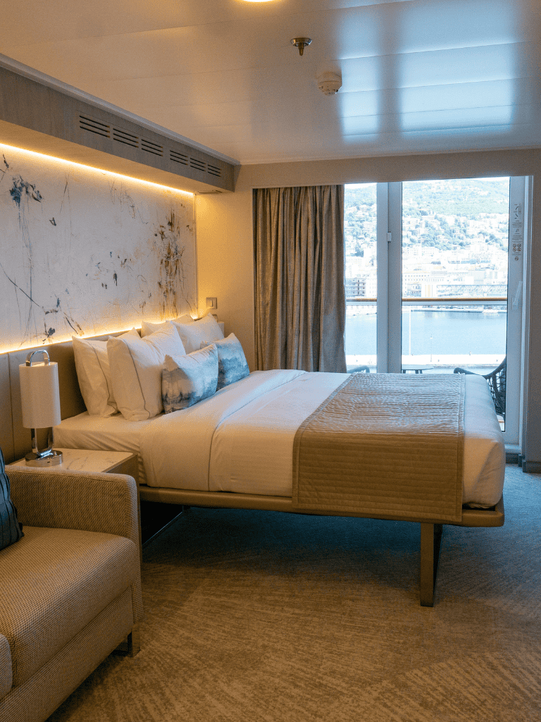 Luxurious hotel room with a view of the city and waterfront, featuring modern decor and cozy bedding.