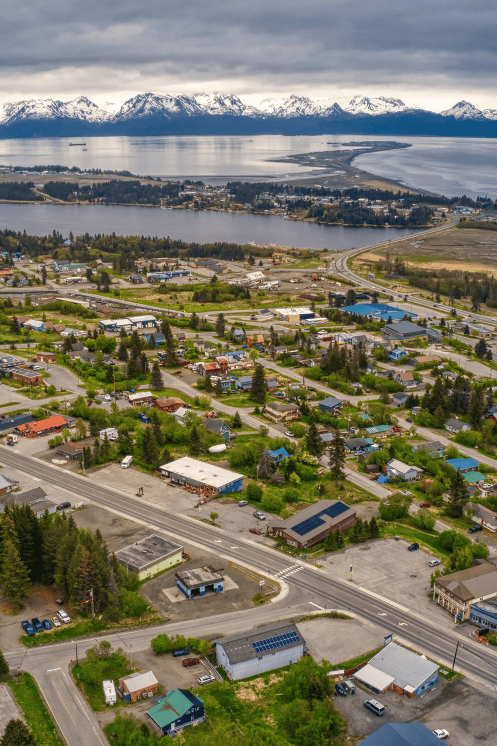 Aerial view of a coastal town with mountains, water, and residential neighborhoods, showcasing scenic landscapes and local community.