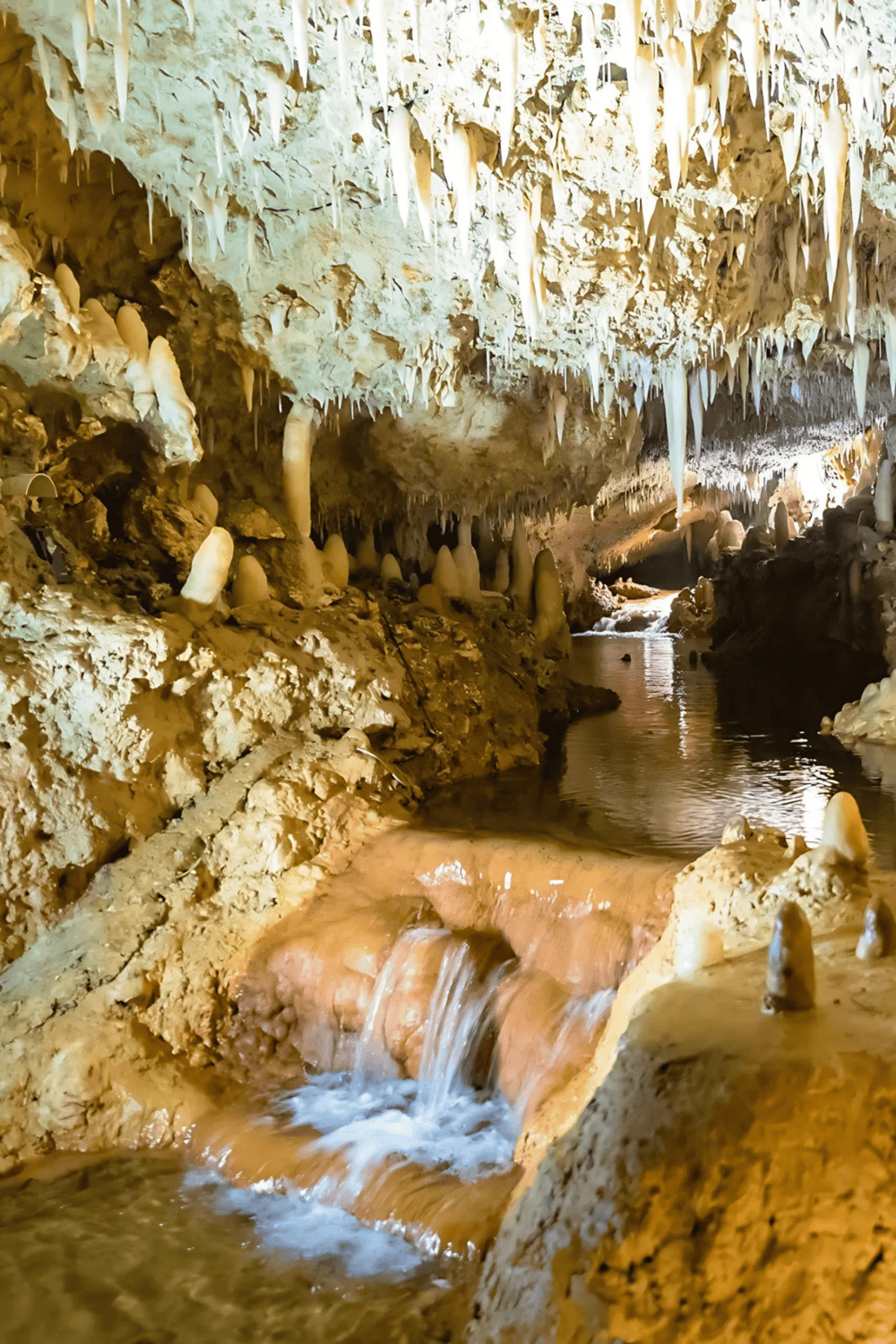 1. Stalactites and stalagmites inside a limestone cave with flowing water, natural cave formations.