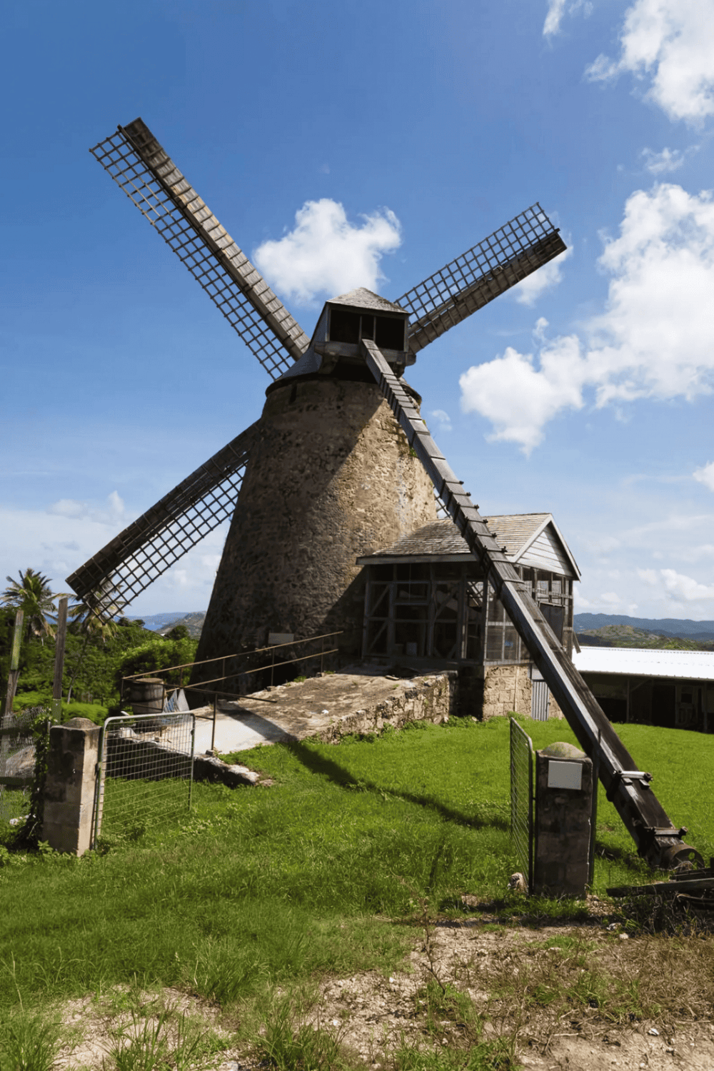 Old stone windmill with wooden sails under blue sky, scenic countryside view, historic attraction, QuestForDirections.