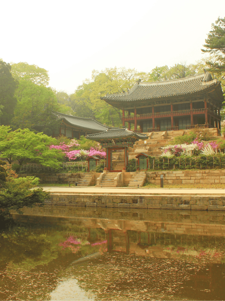 Ancient Korean temple with lush garden and pond reflection, historic architecture, peaceful scenery.