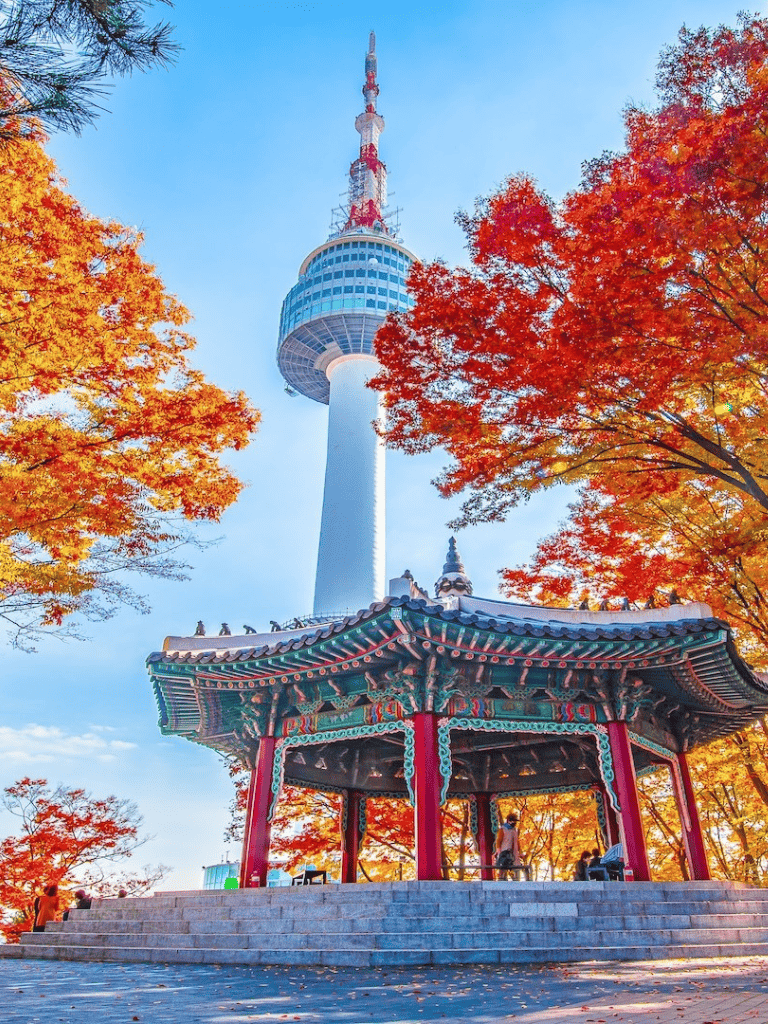 Colorful autumn trees surrounding Seoul Tower and traditional Korean pavilion in Seoul, South Korea.