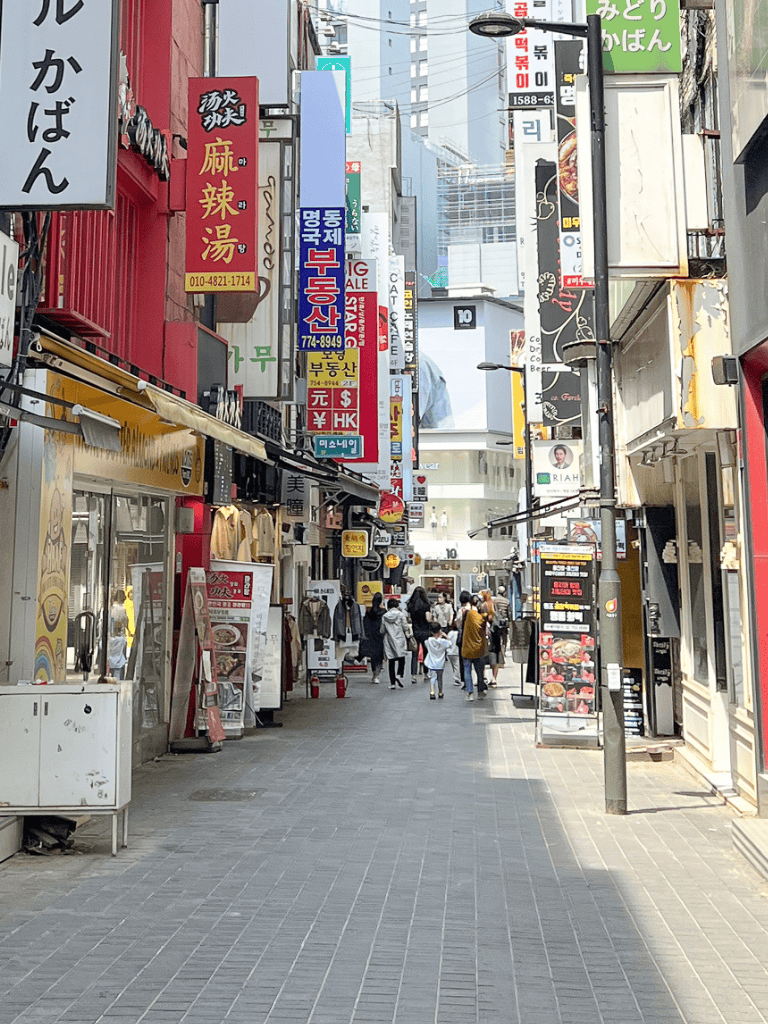 Bustling street scene with diverse shops, bright signs, and pedestrians in an urban area.