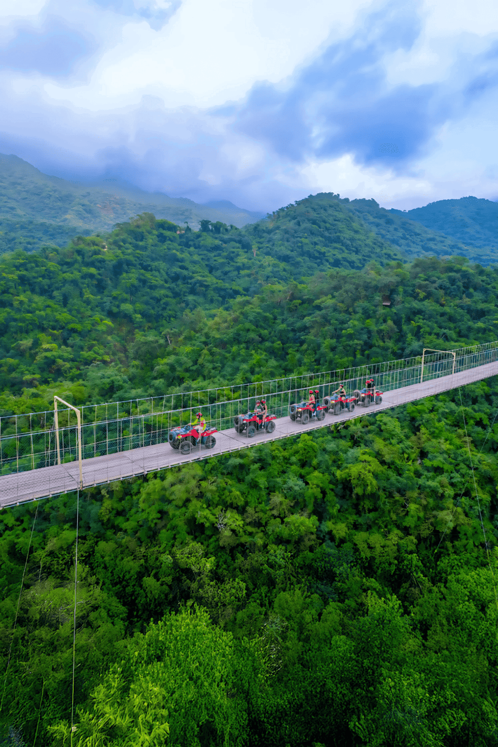 Suspended quad bike adventure over lush green rainforest canopy in tropical mountains.