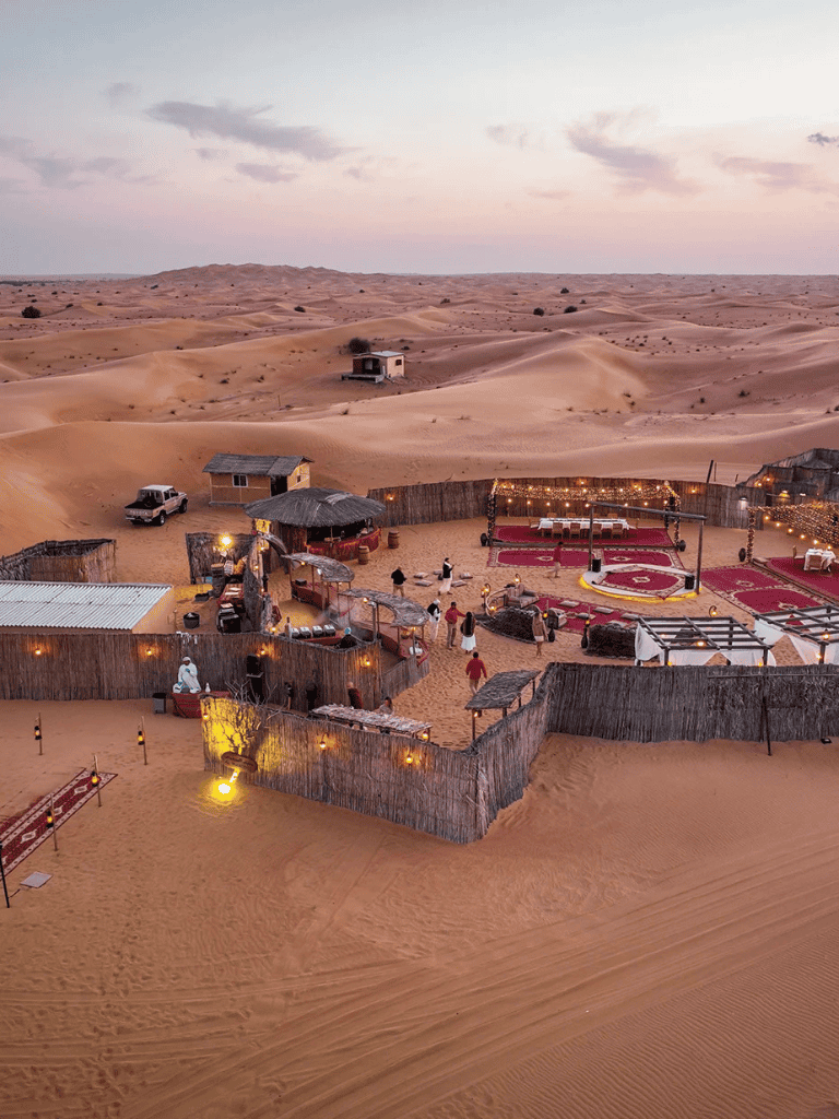 Desert camp with dining and seating areas amid sand dunes at sunset, offering a unique experience with desert exploration.