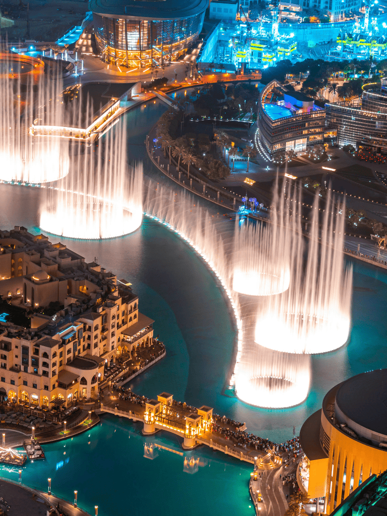 Vibrant Dubai Fountain show at night with illuminated water jets and modern cityscape background.