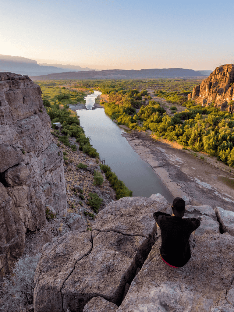 Breathtaking canyon view with a river, lush green trees, and rocky cliffs at sunset.