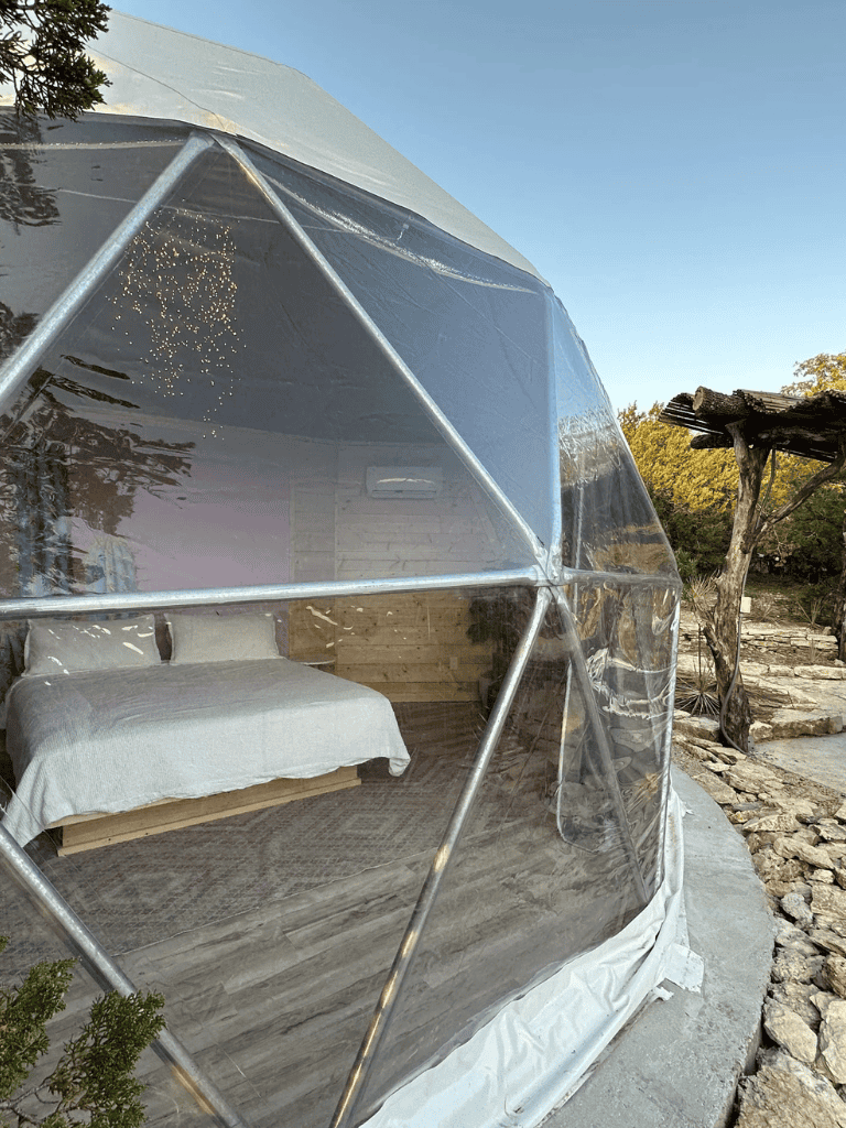 Portable geodesic dome accommodation at QuestForDirections, eco-friendly outdoor lodging, cozy bed inside transparent dome, nature retreat.