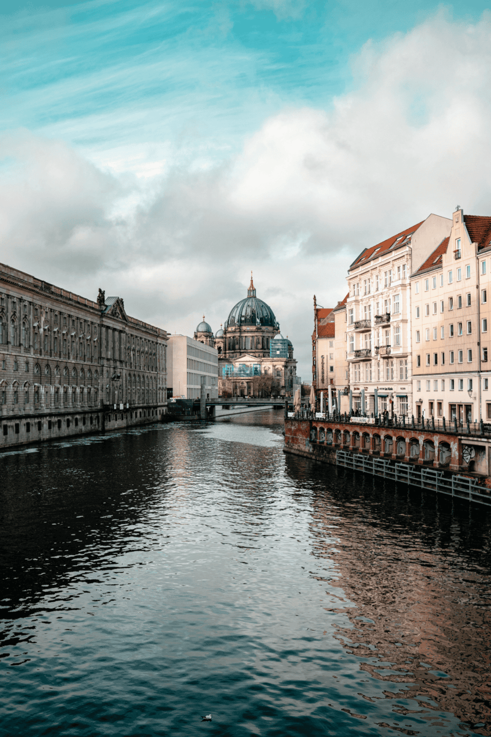 Historic European cityscape with river, classic architecture, and domed church in the background.
