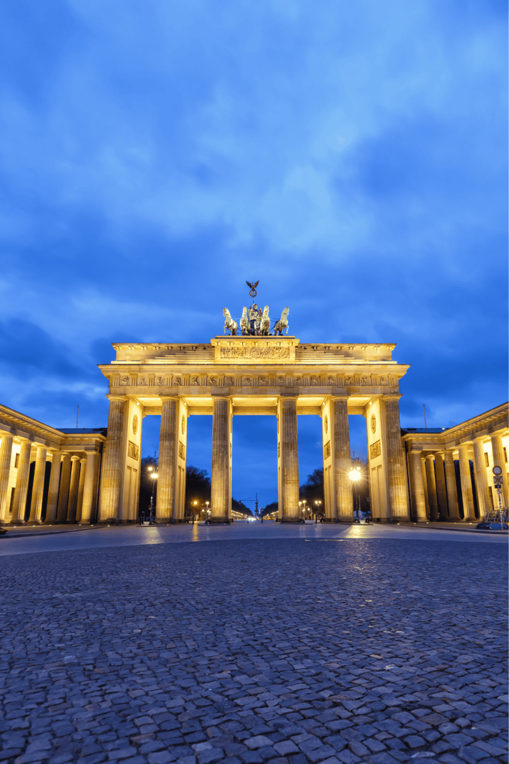 Ancient Berlin Gate at dusk, illuminated with city lights, iconic landmark in Germany's historic capital.