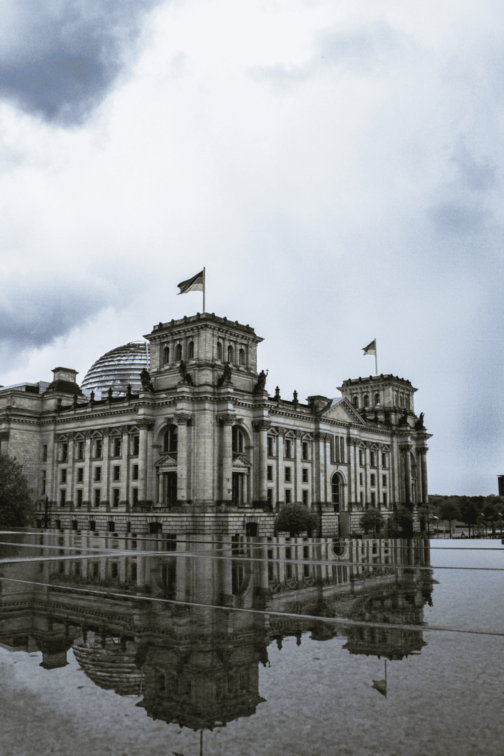 Historic German Parliament Building in Berlin, Reflection in water, cloudy sky, political landmark.