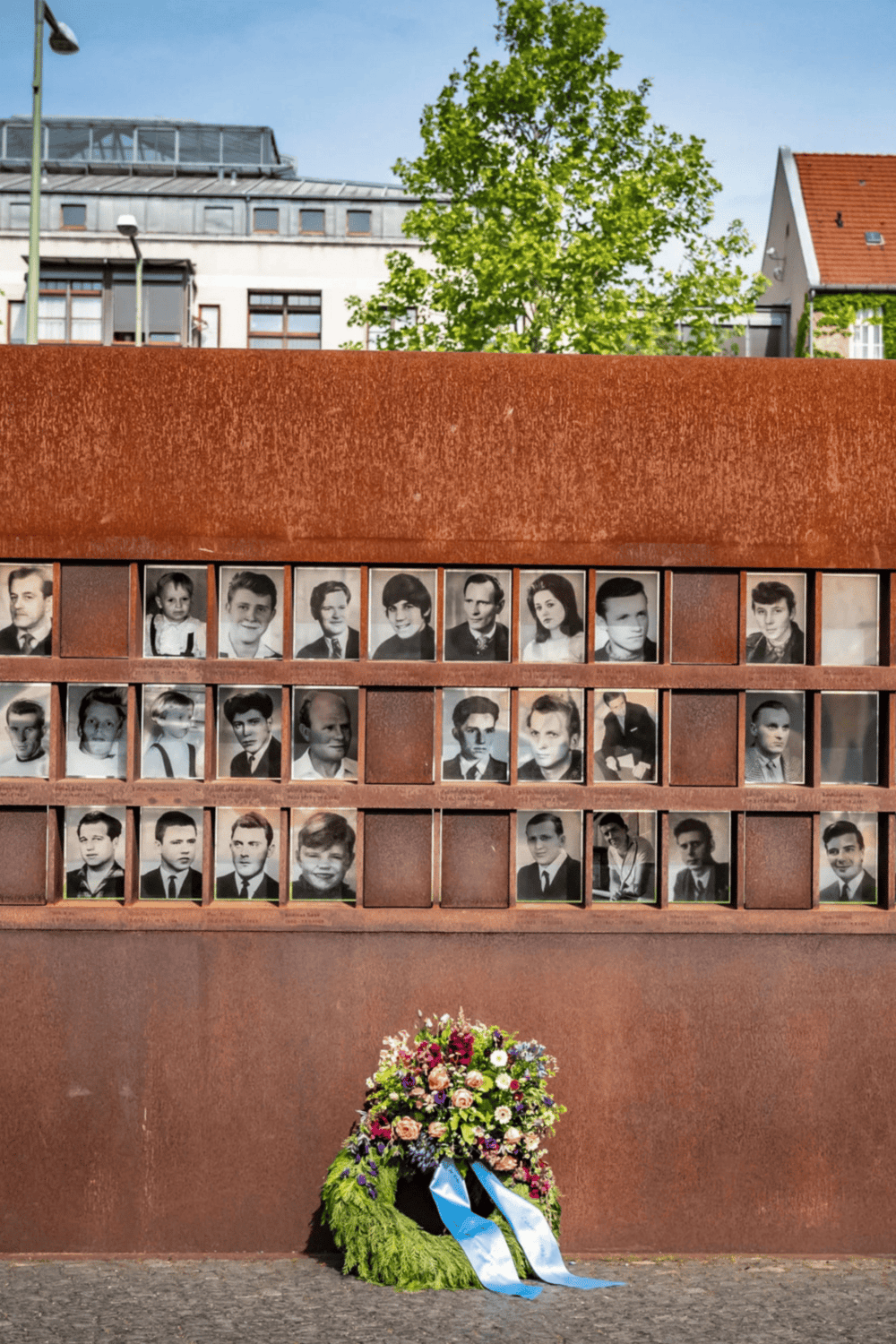 Memorial wall with black and white photos, flowers at the base, honoring past individuals.