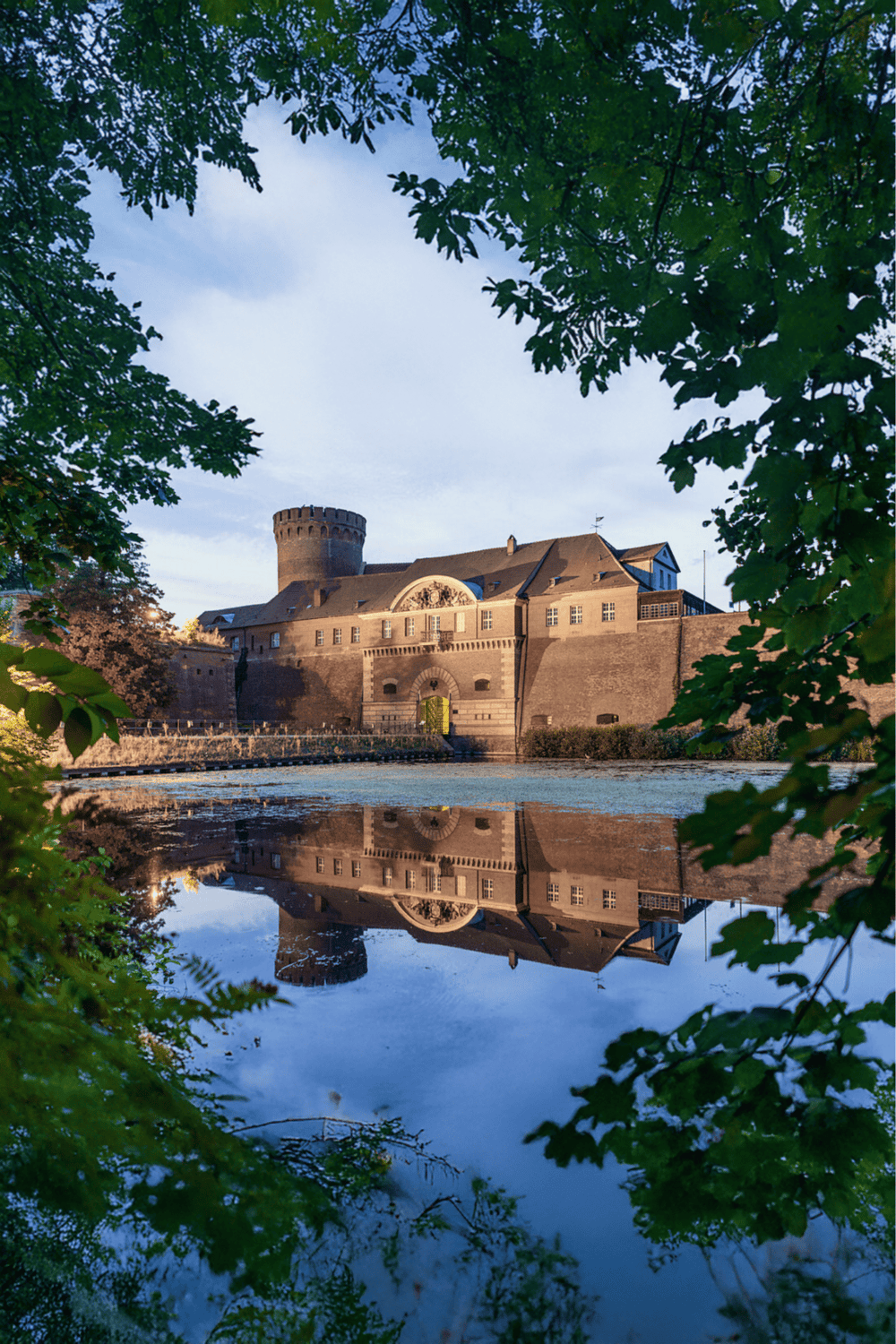 Historic castle near reflecting water, surrounded by greenery, showcasing scenic travel destinations.
