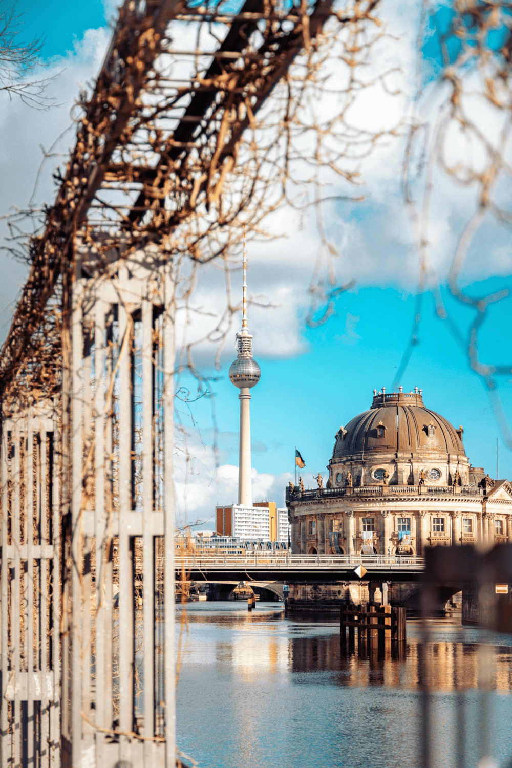 Historic Berlin cityscape with TV Tower, river, and classical architecture under blue sky.