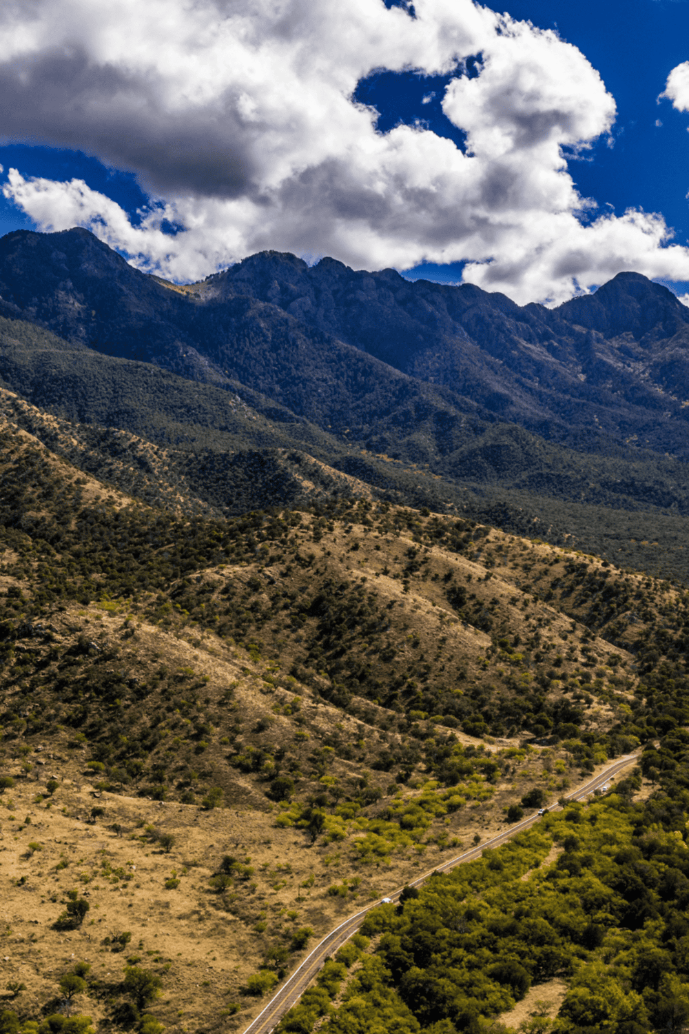 Vast mountain landscape with winding road and lush greenery, scenic outdoor adventure destination.