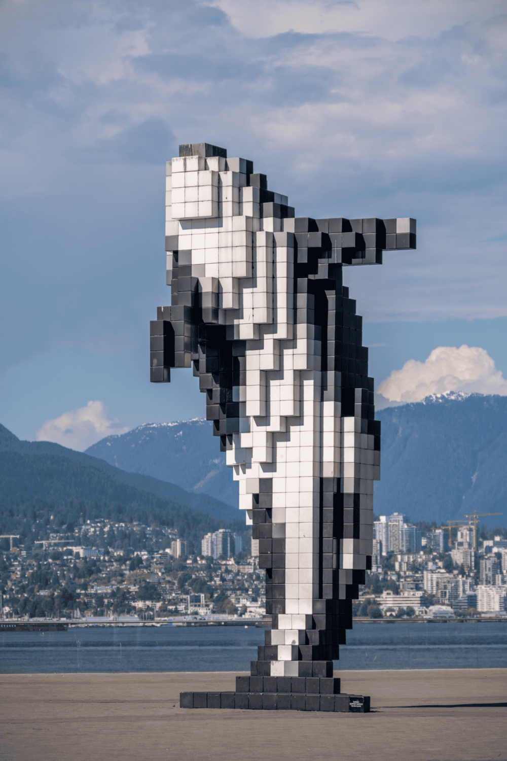 Large pixelated sculpture of a girl with a backpack against city and mountain backdrop.