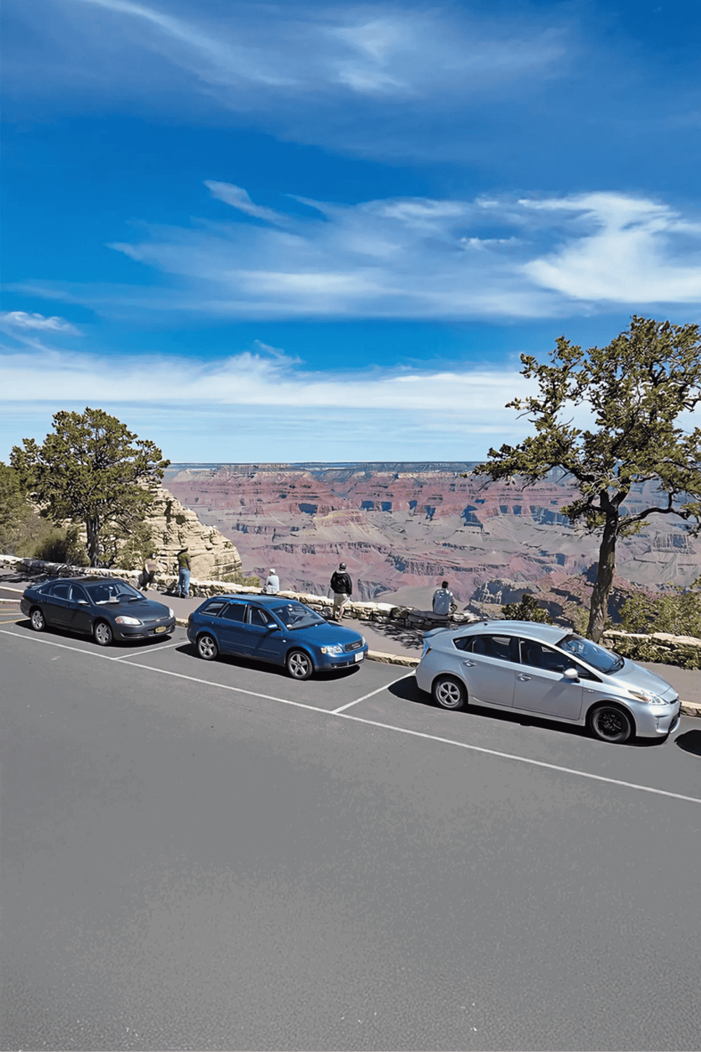 Grand Canyon overlook with parked cars and visitors enjoying scenic view.