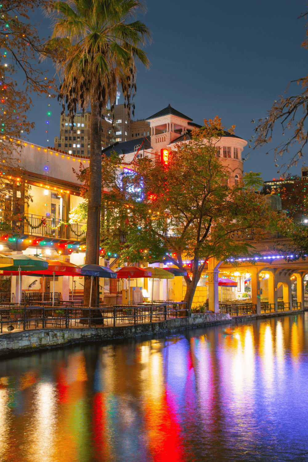 Night scene of San Antonio River Walk with colorful lights, deck, and buildings in downtown, Texas.