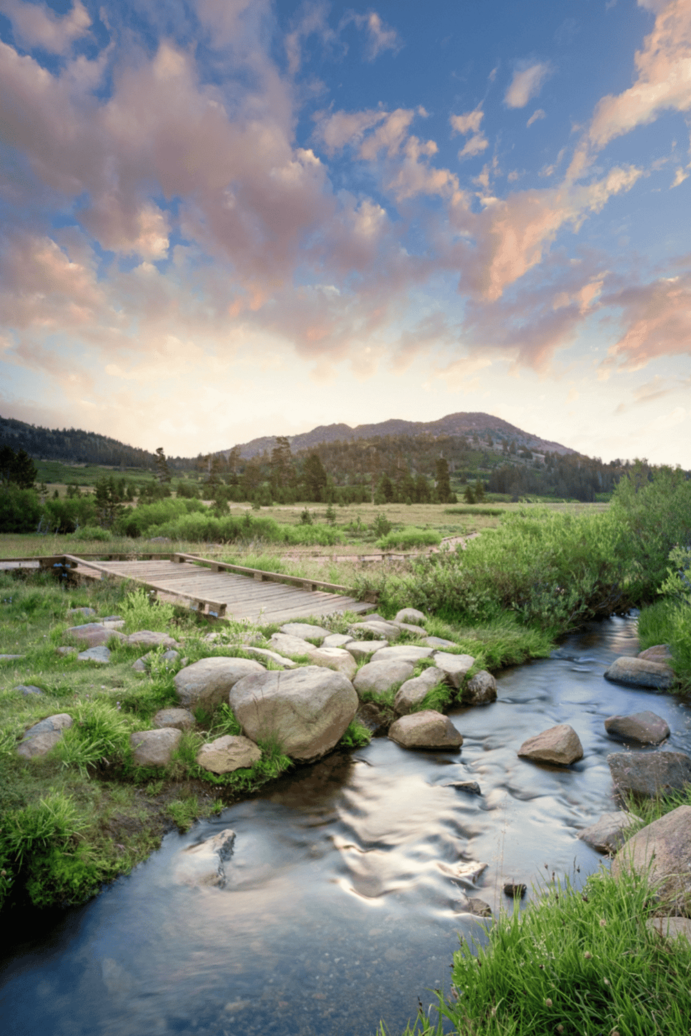 Serene mountain landscape with a flowing stream and wooden bridge at sunset for outdoor adventure.