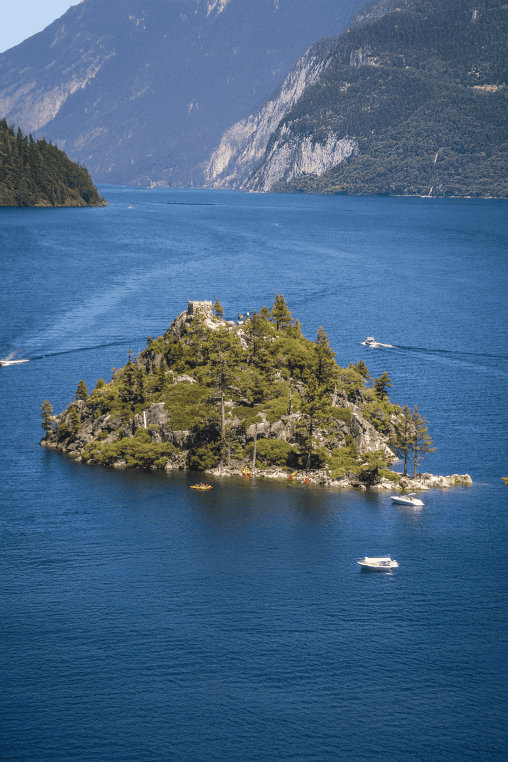 Serene lake with lush island and surrounding mountains, perfect for scenic boat tours and nature exploration.