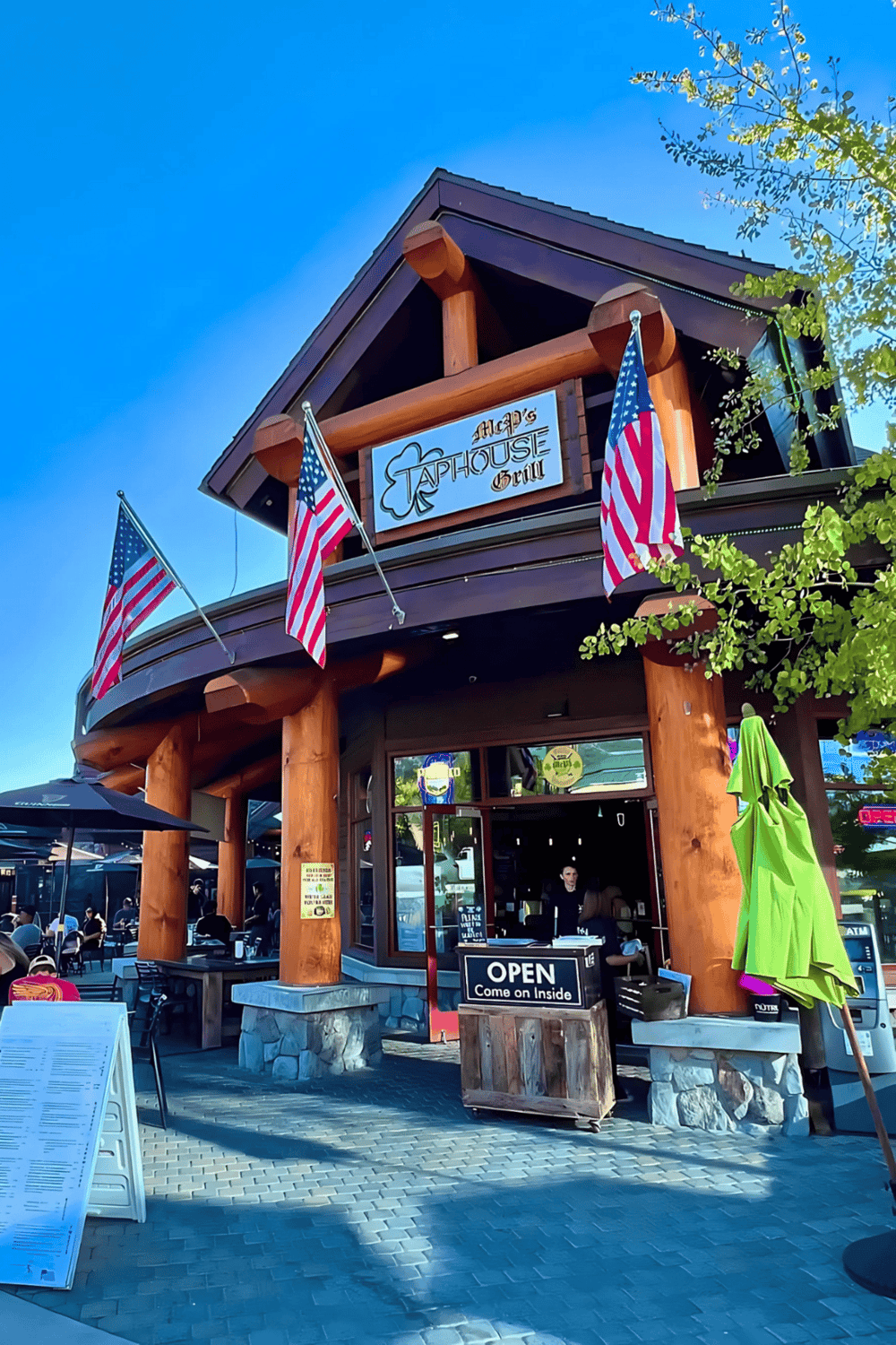 Outdoor dining at a rustic American restaurant with flags and a welcoming sign.