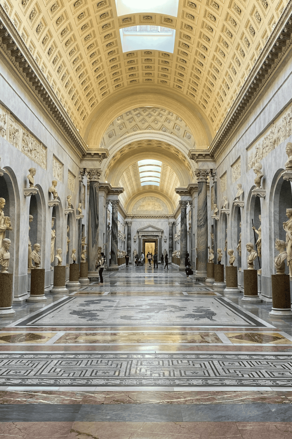 Elegant museum gallery with marble busts, grand arches, and skylights showcasing historical artifacts.