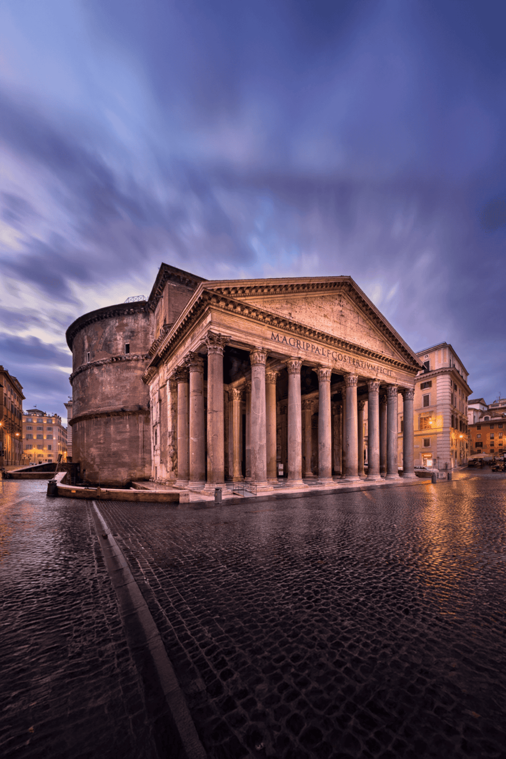 Ancient Roman Pantheon in Rome during sunset with dramatic clouds and cobblestone plaza.