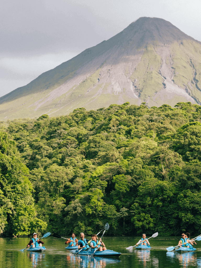 Brightly colored kayaks on a river surrounded by lush green forest, with a towering mountain in the background.