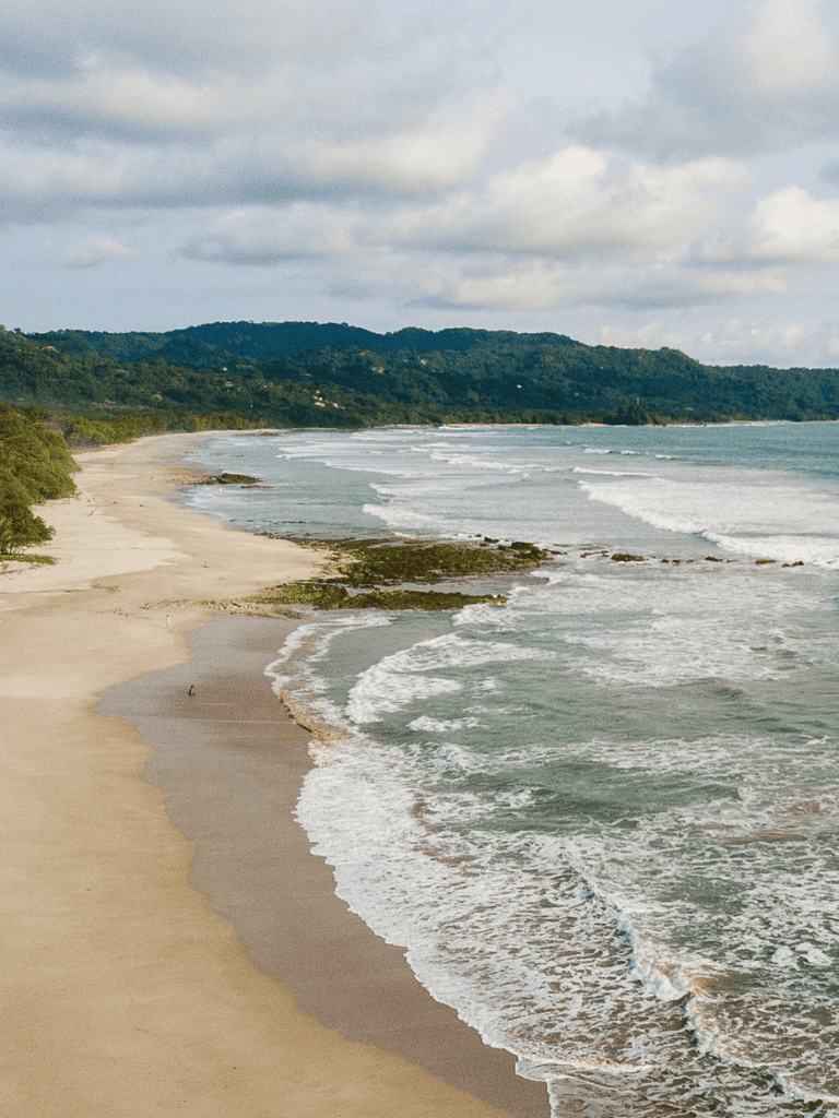 Serene beach with gentle waves and lush green hills in the distance, perfect coastal destination.