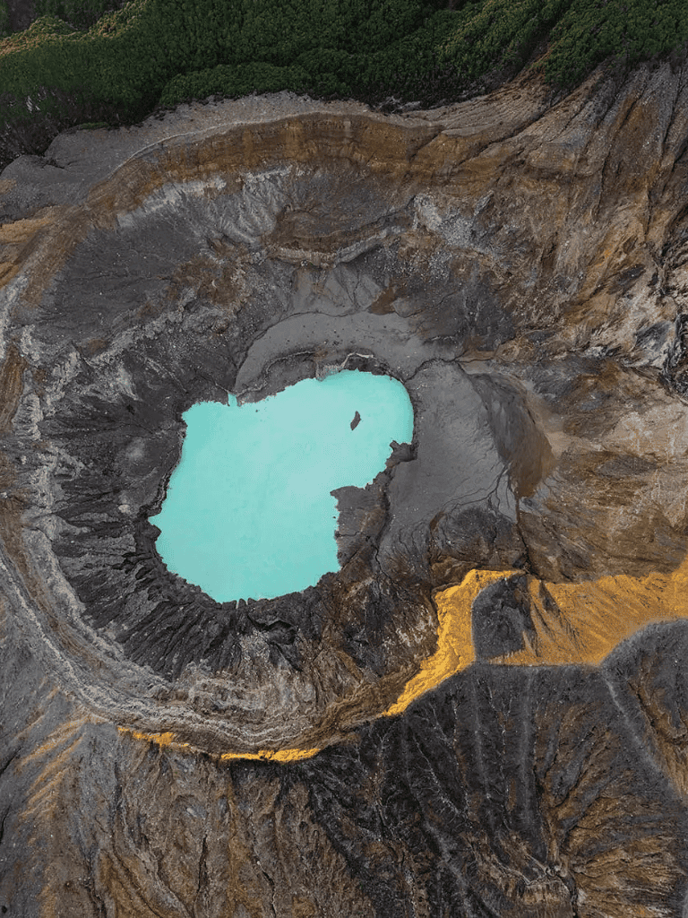 Vast volcanic crater with turquoise crater lake surrounded by rugged volcanic terrain.