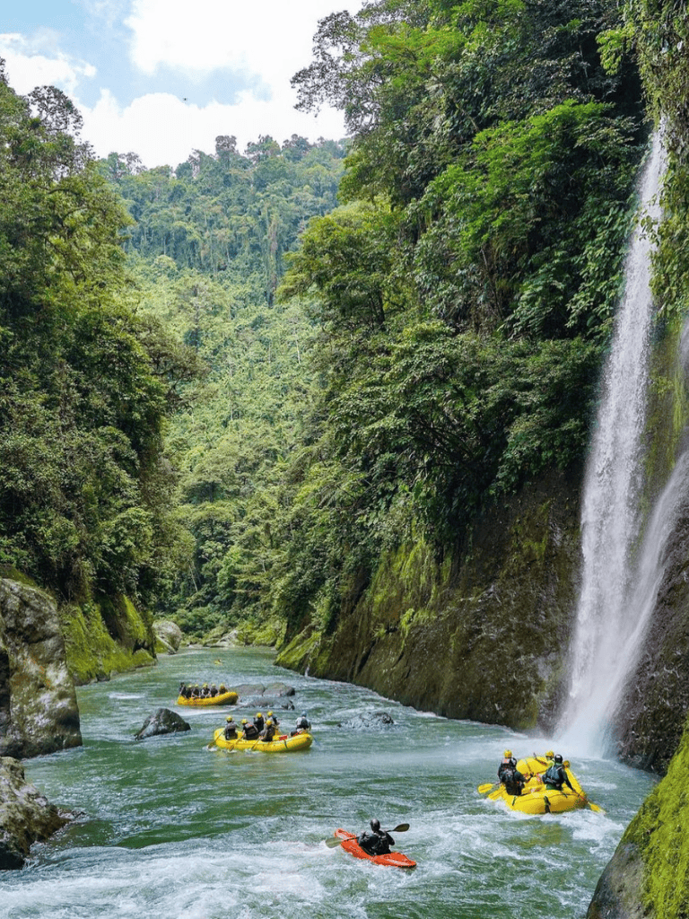 Lush jungle river with rafting adventure and waterfall in a tropical rainforest setting.